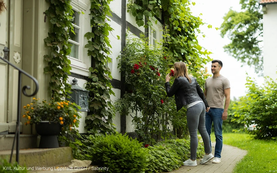 Ausflugsziele Titel Eine Frau atmet den Duft einer Rose vor einem alten Fachwerkhaus am Stift Cappel im Lippstädter Ortsteil Cappel ein. Copyright: KWL Kultur und Werbung Lippstadt GmbH / Sabrinity